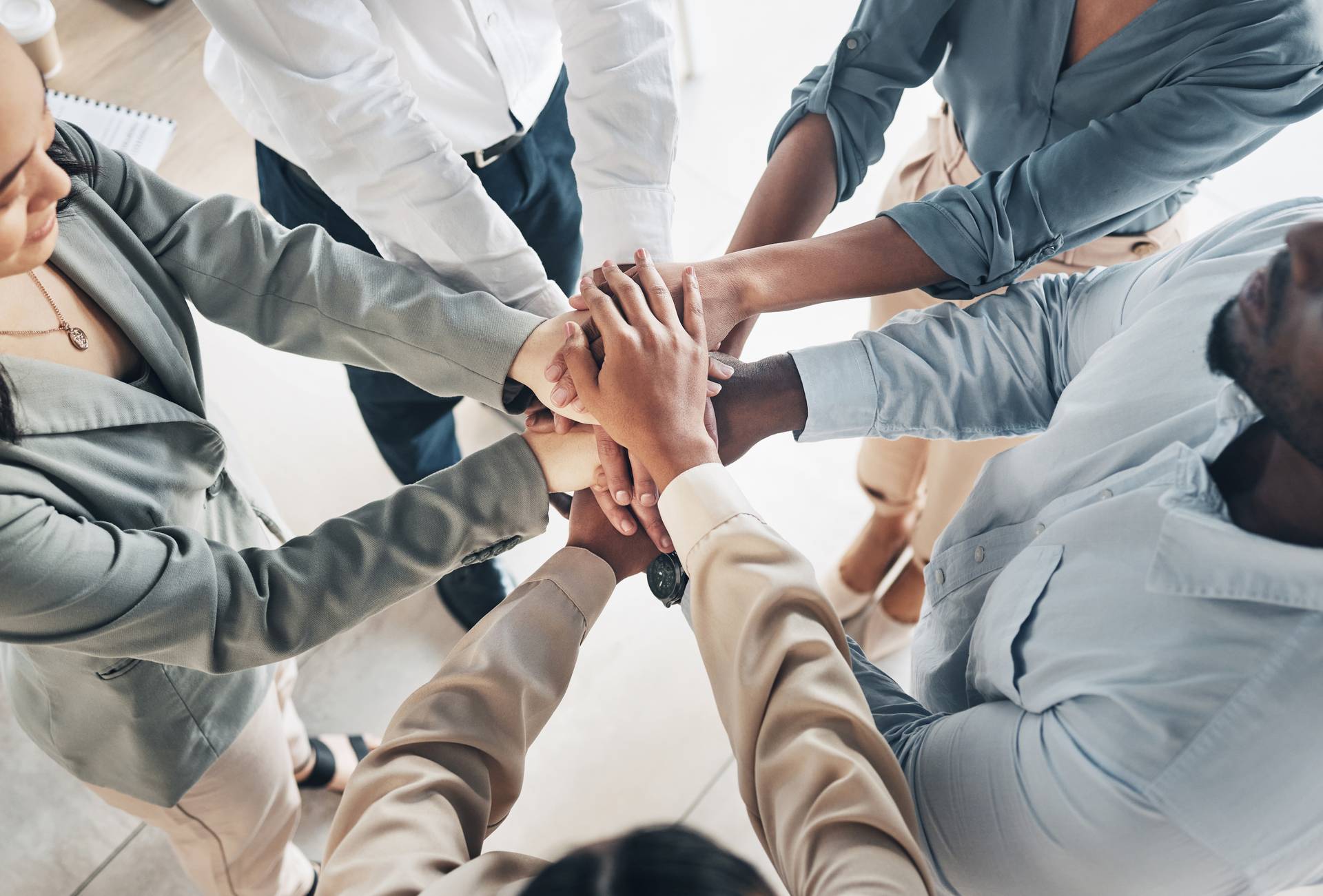 Eine Gruppe von Menschen, die in einem Kreis stehen und ihre Hände in der Mitte zusammenlegen, um Teamwork und Einheit zu symbolisieren.